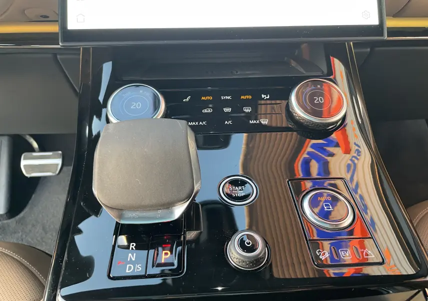 Gros plan sur la console centrale noire brillante du Range Rover Sport P440 HSE R-Dynamic avec commandes de climatisation et levier de vitesses.
