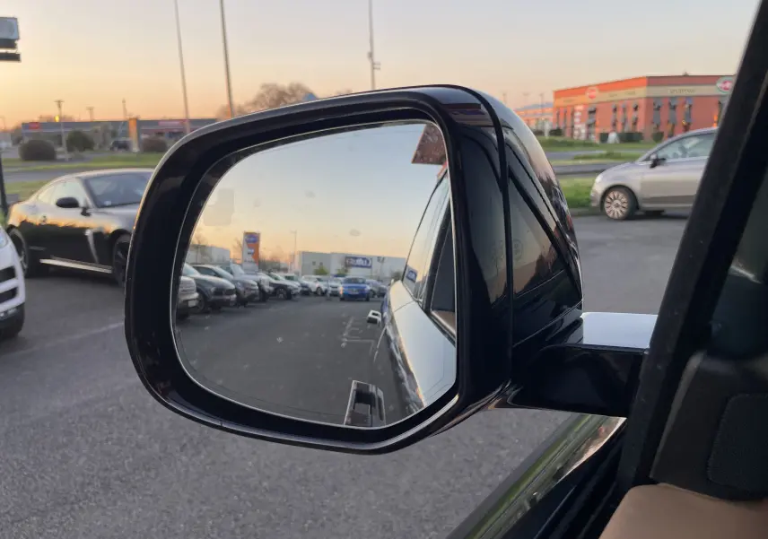 Rétroviseur côté gauche d’un Range Rover Sport P440 HSE R-Dynamic Carpathian Grey, reflet d’un parking au crépuscule.