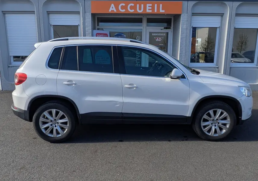 Vue de profil côté gauche d'un Volkswagen Tiguan blanc garé devant un bâtiment commercial.