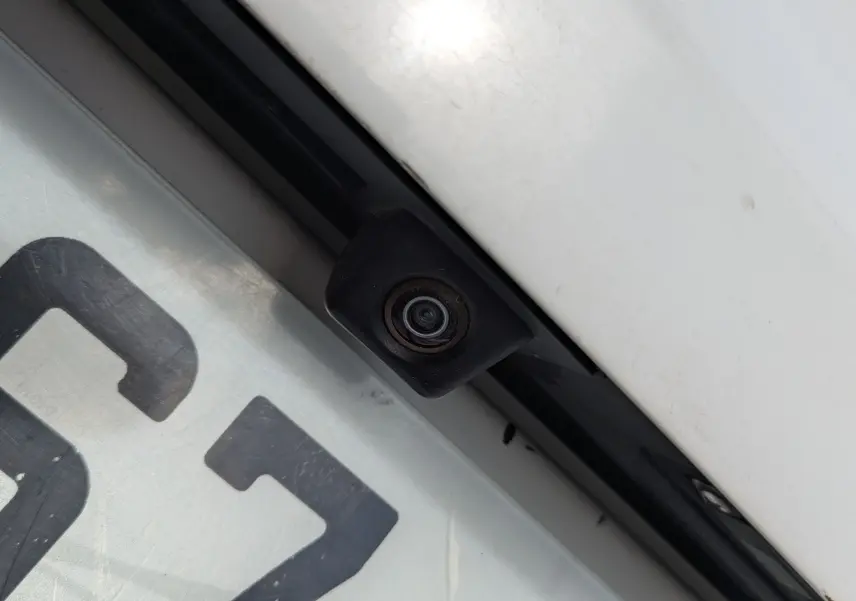 Gros plan sur la caméra de recul noire intégrée au-dessus de la plaque d’immatriculation d’un Volkswagen Tiguan blanc.