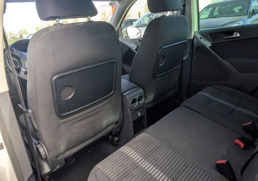 Vue intérieure arrière du Volkswagen Tiguan 2010, sièges noirs avec motifs rayés et porte ouverte côté gauche.