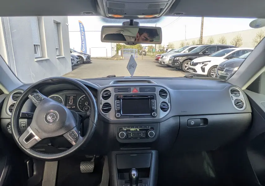 Vue intérieure avant du Volkswagen Tiguan 2010 avec tableau de bord noir et sièges tissu rayés gris.