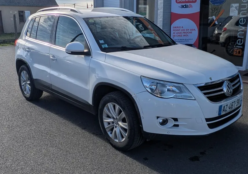 Volkswagen Tiguan blanc vu en 3/4 avant droit, avec jantes alu et toit ouvrant, devant un bâtiment commercial.