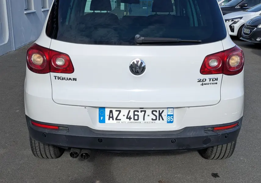 Vue arrière d'un Volkswagen Tiguan blanc avec plaques françaises et feux arrière allumés, stationné en extérieur.