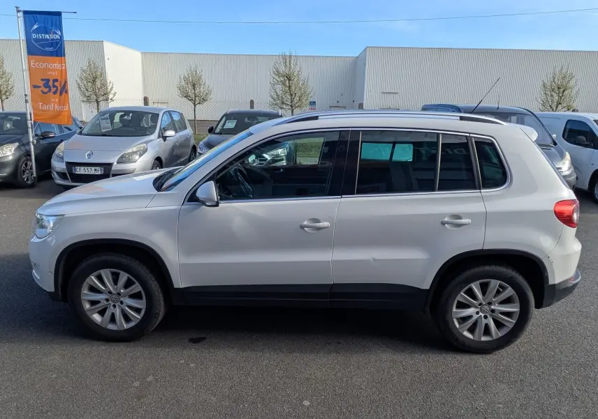 Vue de profil côté gauche d'un Volkswagen Tiguan blanc 2010 avec jantes alliage, sur parking extérieur.