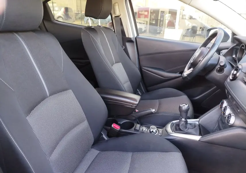 Vue intérieure côté conducteur de la Mazda2 2018 avec sièges tissu noir et console centrale avec boîte manuelle.