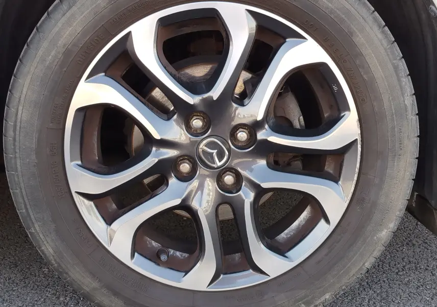 Gros plan sur la roue avant droite d'une Mazda2 blanche avec jante alliage et pneu visible sur sol asphalté.