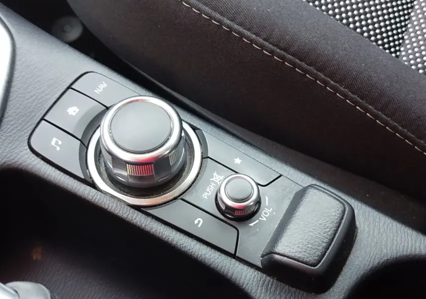Vue rapprochée du système de commande multimédia central noir sur la console intérieure de la Mazda2 blanche.