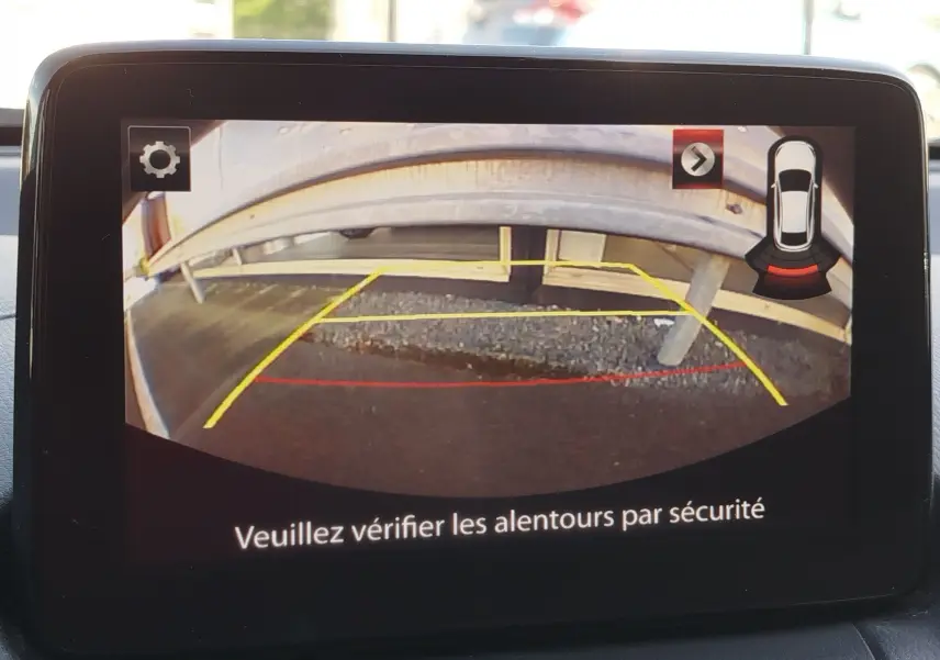 Écran de caméra de recul d'une Mazda2 blanche, montrant une barrière métallique vue de l'arrière du véhicule.