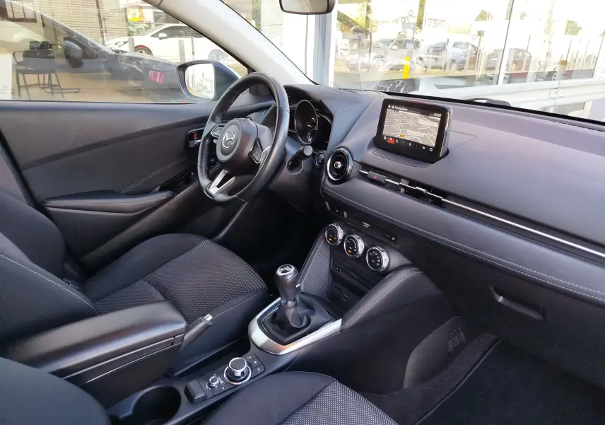 Vue intérieure côté conducteur de la Mazda2 2018 avec tableau de bord noir et écran tactile central affichant la navigation.