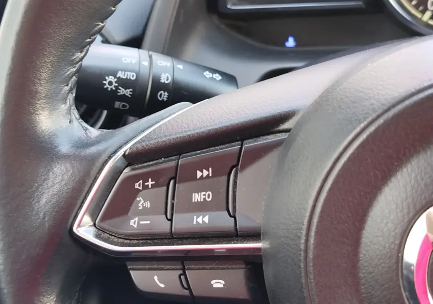 Gros plan sur les commandes au volant à gauche du Mazda2 blanc, avec boutons de volume et gestion multimédia visibles.