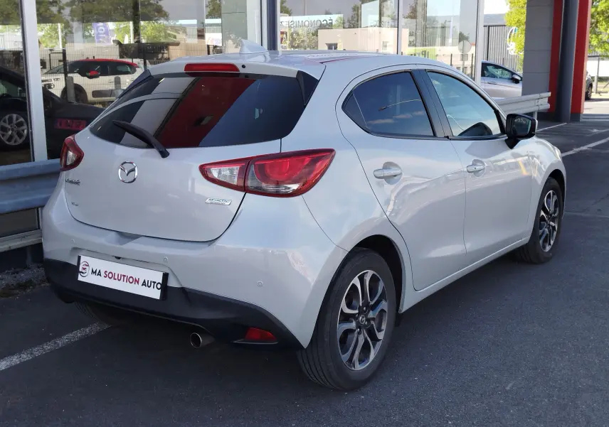 Vue 3/4 arrière droite d'une Mazda2 blanche nacrée avec vitres teintées et jantes alliage bicolores.
