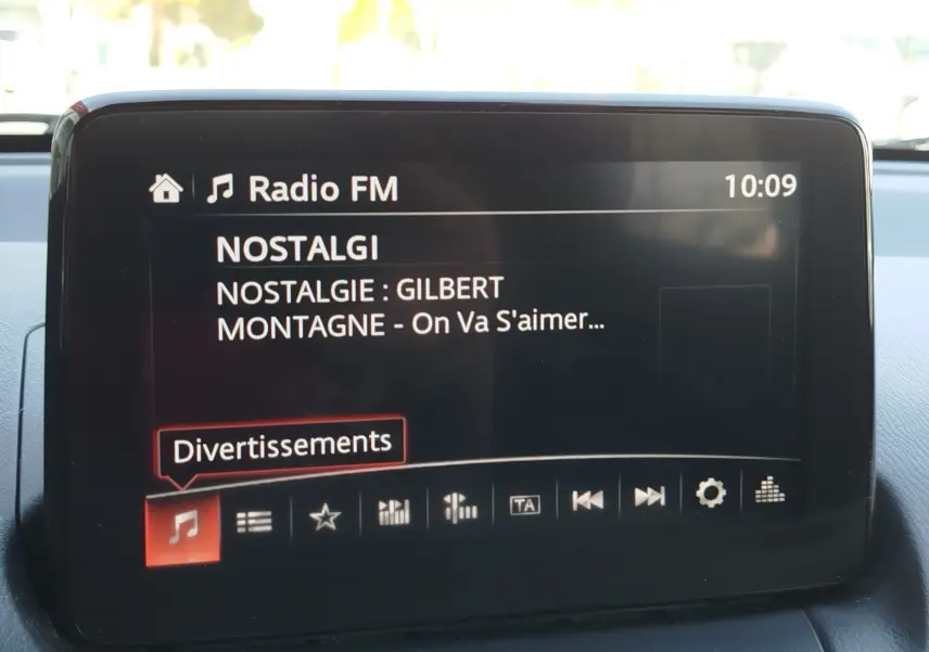 Écran central de la Mazda2 affichant la radio FM sur la station Nostalgie, intérieur gris visible.