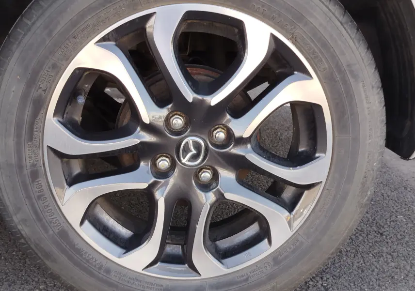 Gros plan sur la jante alliage bi-ton noir et argent avec logo Mazda, roue avant droite d'une Mazda2 blanche.