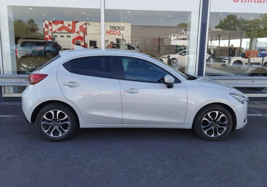 Vue latérale droite d'une Mazda2 blanche nacrée 2018, avec jantes alliage bicolores et vitres teintées.