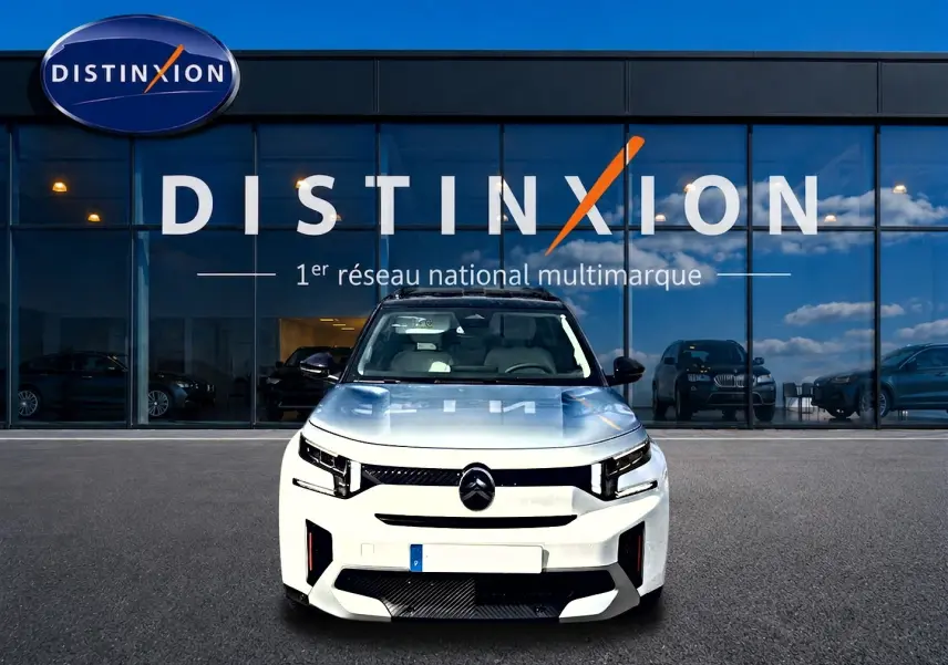 Vue frontale d'un Citroën C3 Aircross blanc 2026 avec calandre noire et toit panoramique, devant un showroom Distinxion.