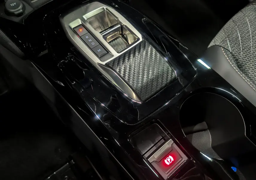 Vue rapprochée de la console centrale noire brillante du Peugeot 2008 Hybrid 145 avec levier de vitesses automatique et frein à main électronique.