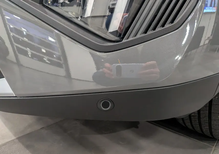 Gros plan sur le pare-chocs avant gris Sélénium du Peugeot 2008 Hybrid 145 e-DCS6 Allure avec capteur de stationnement visible.