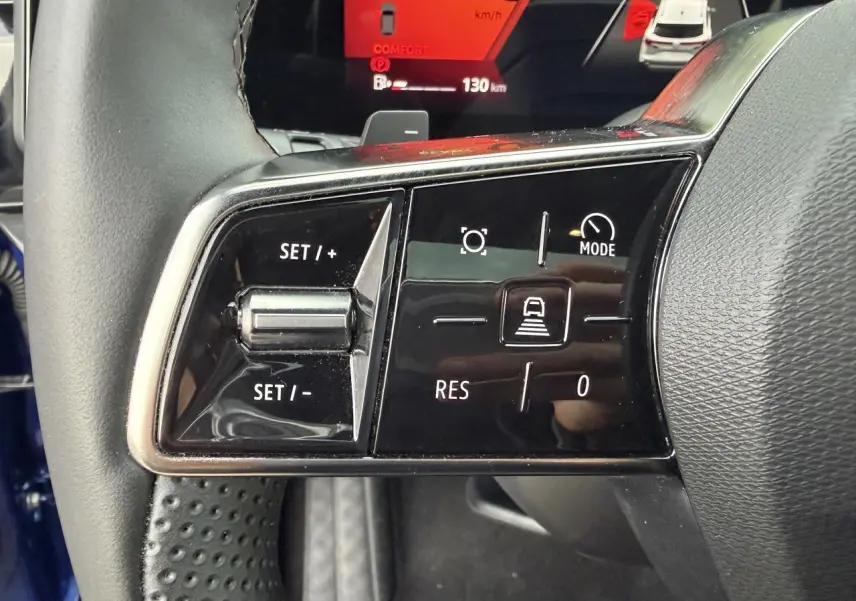 Gros plan sur les commandes au volant gauche du Renault Austral bleu, avec affichage digital rouge en arrière-plan.