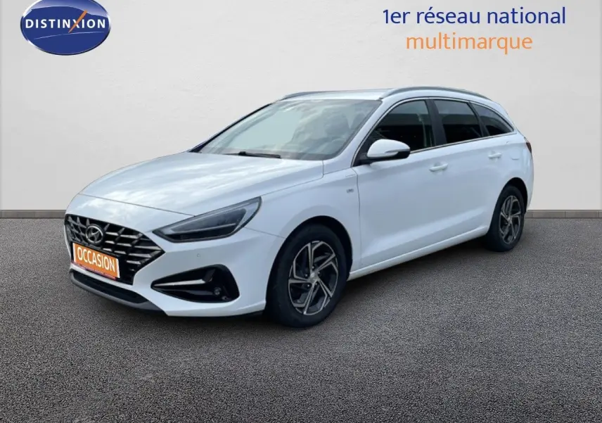 Vue 3/4 avant droite d'une Hyundai i30 SW 2022 en blanc Atlas avec jantes alliage et calandre noire distinctive.