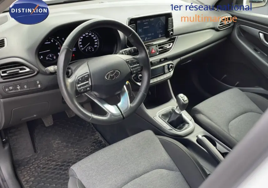 Vue intérieure côté conducteur de la Hyundai i30 SW 2022, volant cuir multifonction et sellerie tissu gris.