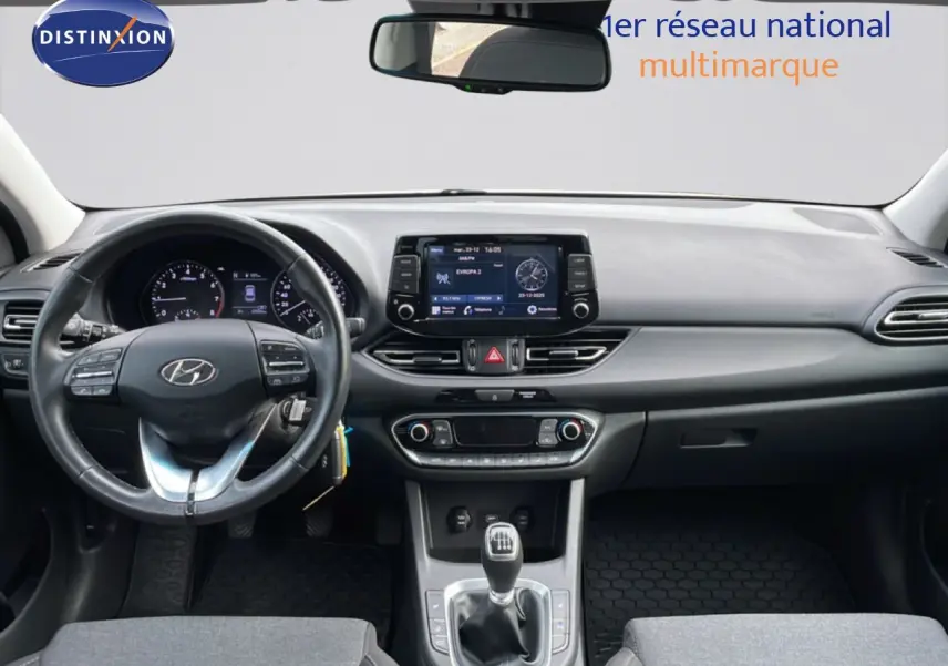 Vue intérieure avant de la Hyundai i30 SW 2022, tableau de bord noir avec volant cuir et levier de vitesse manuel.