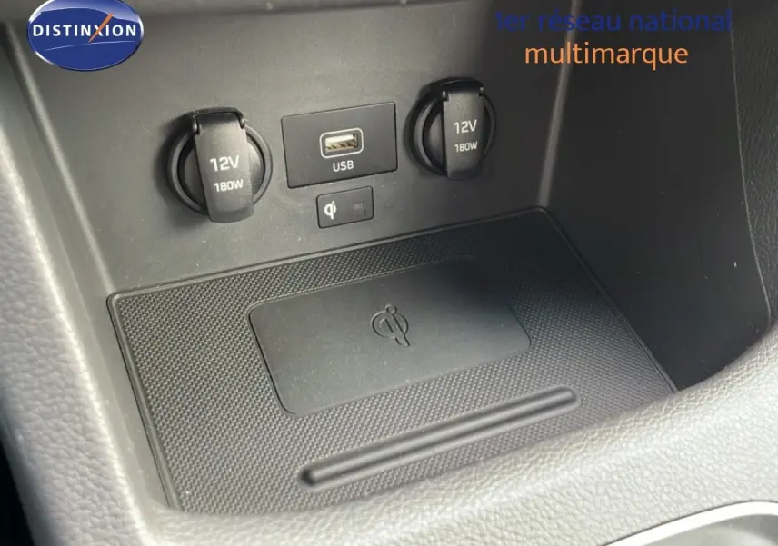 Gros plan sur la console centrale du Hyundai i30 SW blanc, montrant prises 12V, port USB et zone de recharge sans fil.