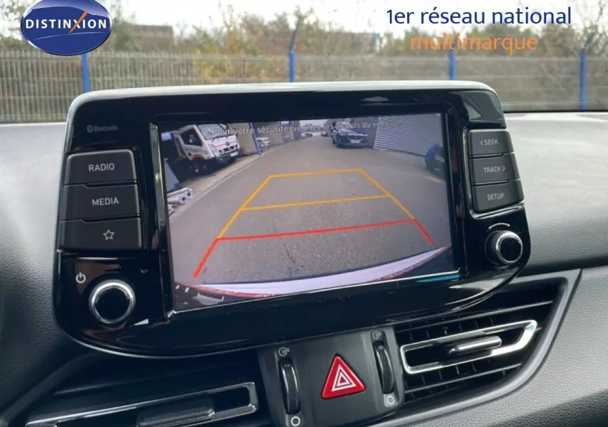 Écran central de la Hyundai i30 SW blanc montrant la caméra de recul avec guidage coloré dans un parking.