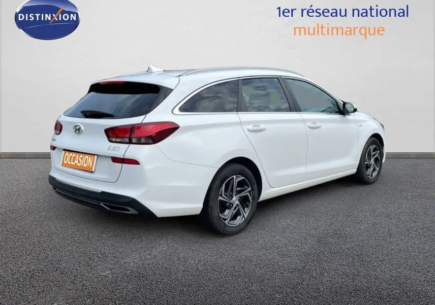 Vue 3/4 arrière droite d'une Hyundai i30 SW blanche Atlas, break compact avec vitres teintées et jantes alliage.