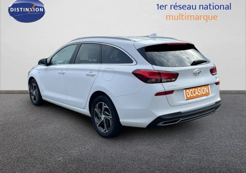 Vue 3/4 arrière droite d'une Hyundai i30 SW blanche Atlas, break compact avec feux arrière rouges et jantes alliage.