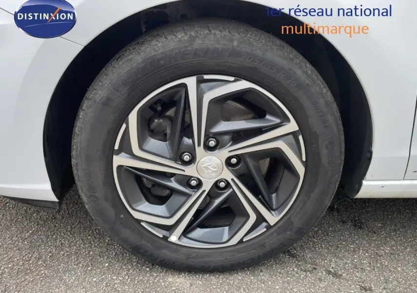 Gros plan sur la roue avant gauche d'une Hyundai i30 SW blanche, avec jante alliage au design géométrique moderne.