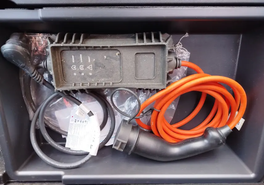 Câble de recharge orange et boîtier de contrôle pour Peugeot 3008 Hybrid 225ch, vue rapprochée dans un compartiment.