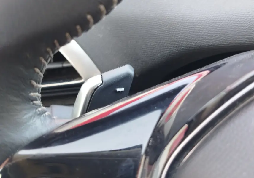 Gros plan sur la palette de changement de vitesse derrière le volant en cuir noir du Peugeot 3008 hybride.