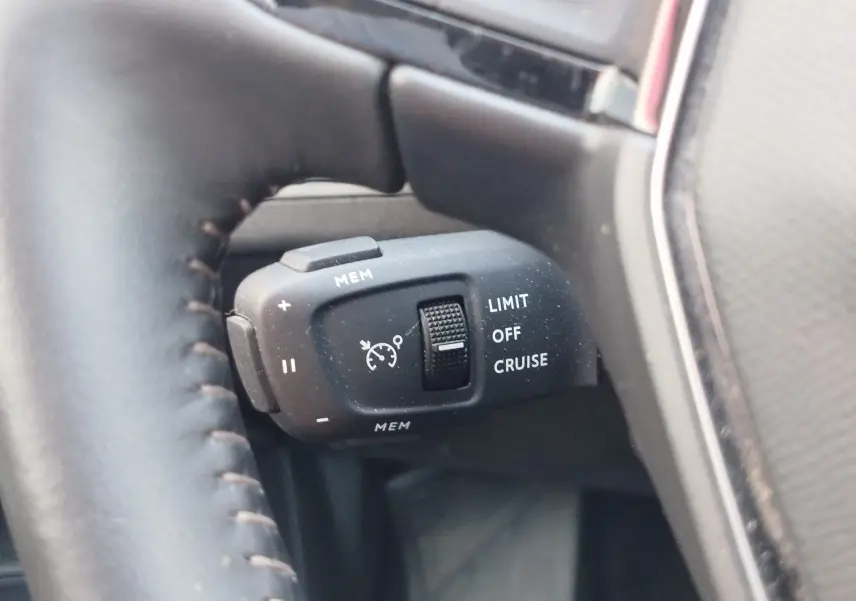 Gros plan sur la commande de régulateur de vitesse au volant cuir noir du Peugeot 3008 Hybrid 225ch bleu Célèbes.