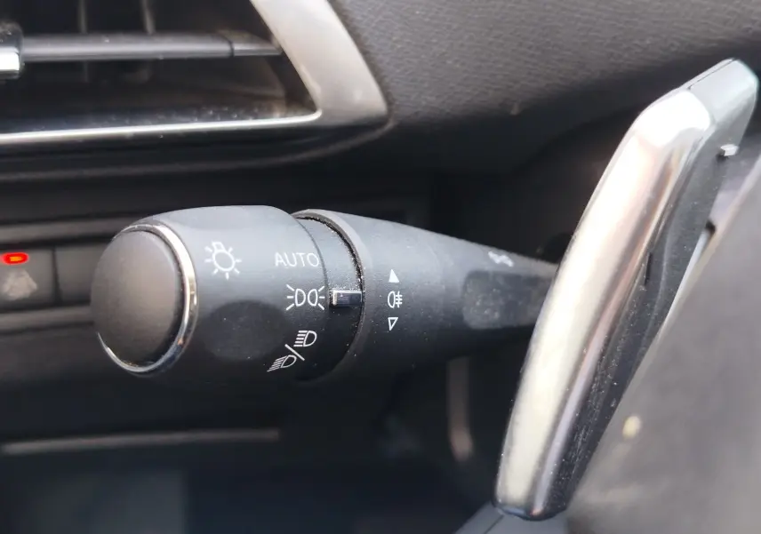 Gros plan sur la commande des phares noire à gauche du volant dans l’habitacle du Peugeot 3008 Hybrid 225ch bleu Célèbes.