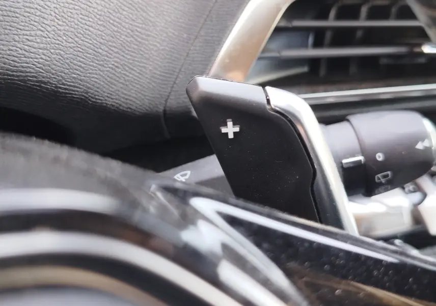 Gros plan sur la palette de changement de vitesse + au volant noir du Peugeot 3008 Hybrid 225ch 2022, intérieur moderne.