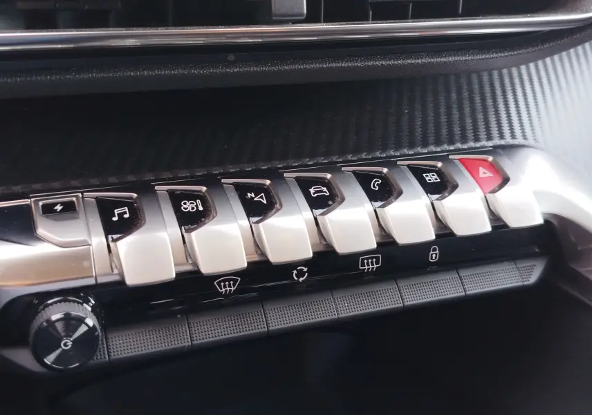 Gros plan sur la rangée de boutons argentés et noirs du tableau de bord du Peugeot 3008 bleu, avec bouton rouge d’alerte visible.