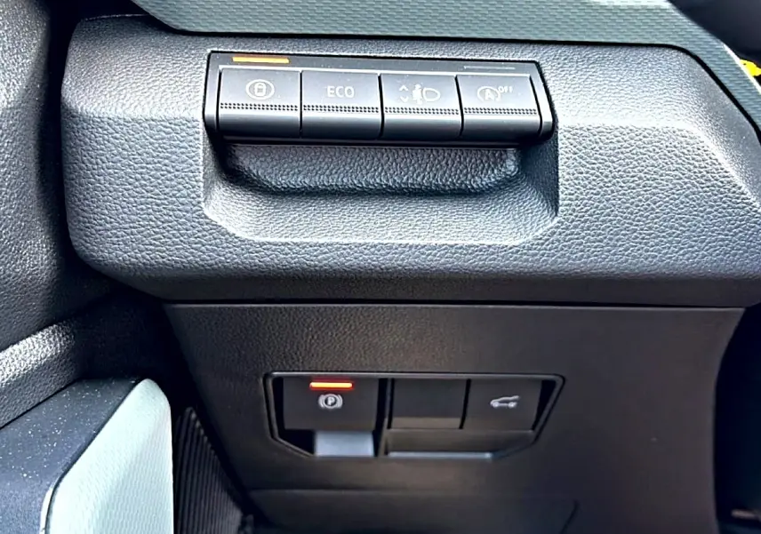 Gros plan sur les commandes noires du tableau de bord du Dacia Bigster, avec bouton Eco et frein à main électronique.