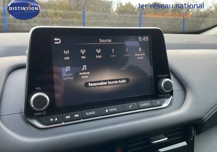Écran tactile central du Nissan Qashqai 2023 affichant les options audio avec tableau de bord noir et coutures blanches.