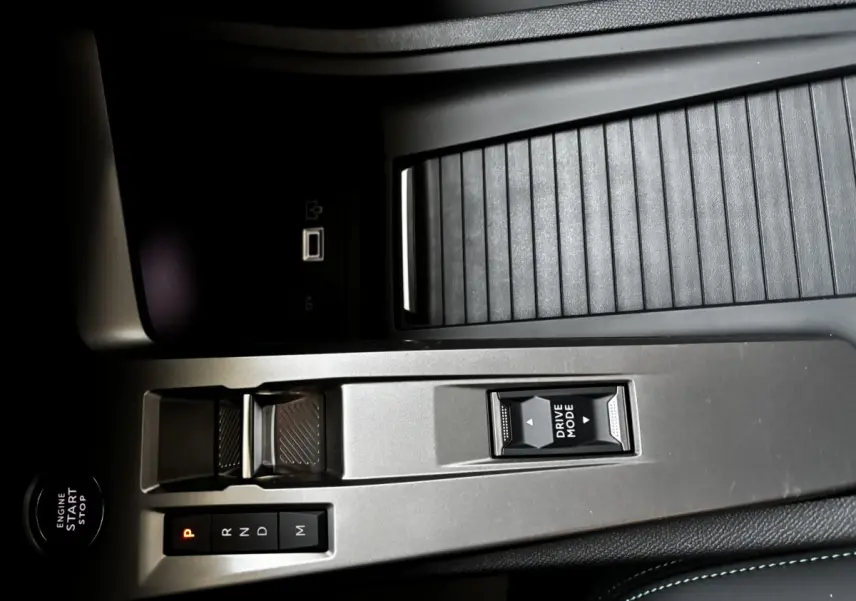 Vue rapprochée de la console centrale de la Peugeot 308 Hybrid 136 e-DCS6 Allure 2025, avec commandes boîte auto et bouton Drive Mode.