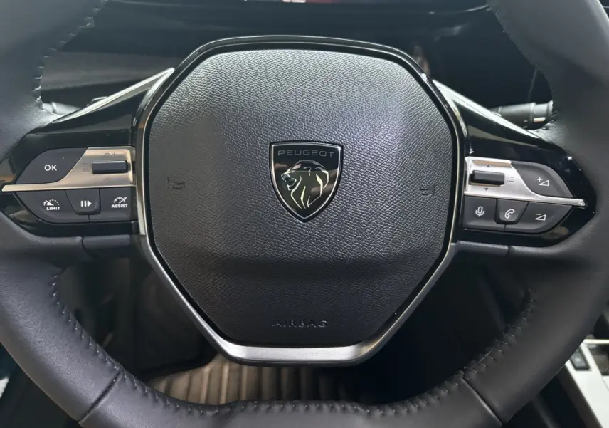 Gros plan sur le volant cuir noir multifonctions de la Peugeot 308 Hybrid 2025 avec logo lion central.