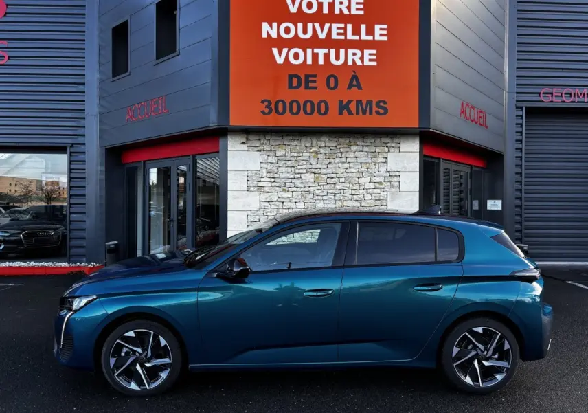 Profil côté gauche d'une Peugeot 308 Hybrid 136 e-DCS6 Allure bleu métallisé, garée devant un bâtiment avec panneau orange.