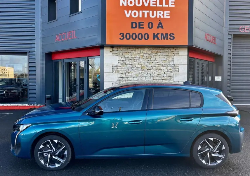 Profil droit d'une Peugeot 308 Hybrid 136 e-DCS6 Allure bleu métallisé, garée devant un bâtiment avec enseigne orange.