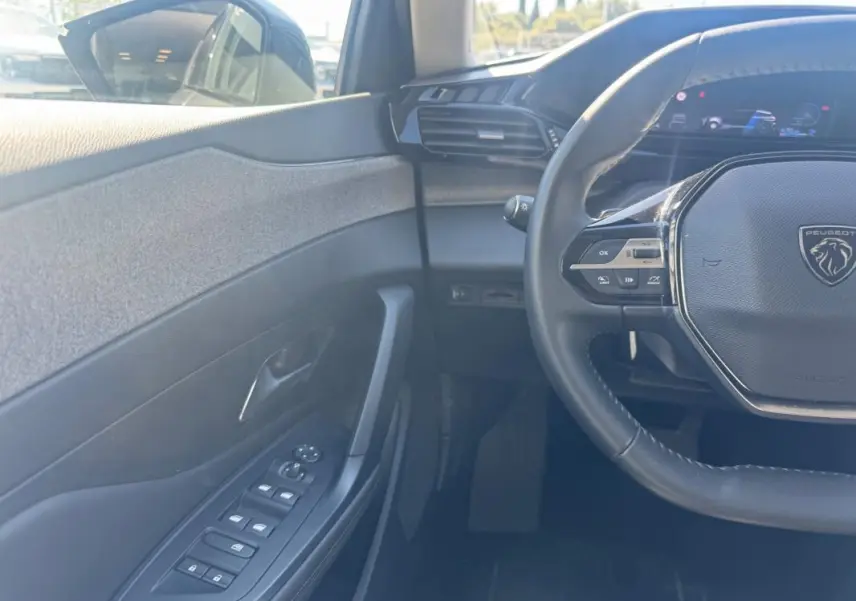 Vue intérieure côté conducteur de la Peugeot 308 Hybrid gris, avec volant multifonction et commandes des vitres électriques.