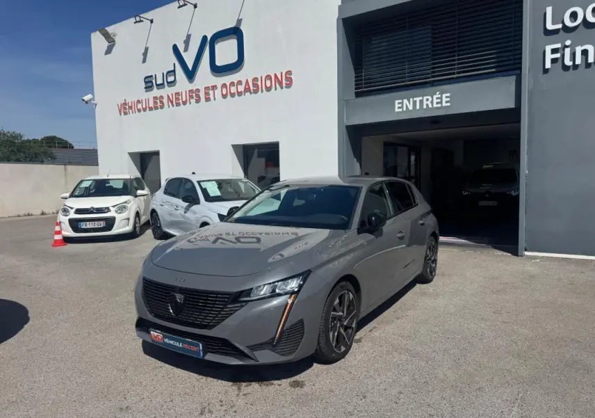 Peugeot 308 Hybrid gris vue 3/4 avant droit, jantes alliage 17 pouces, stationnée devant un garage Sud VO.
