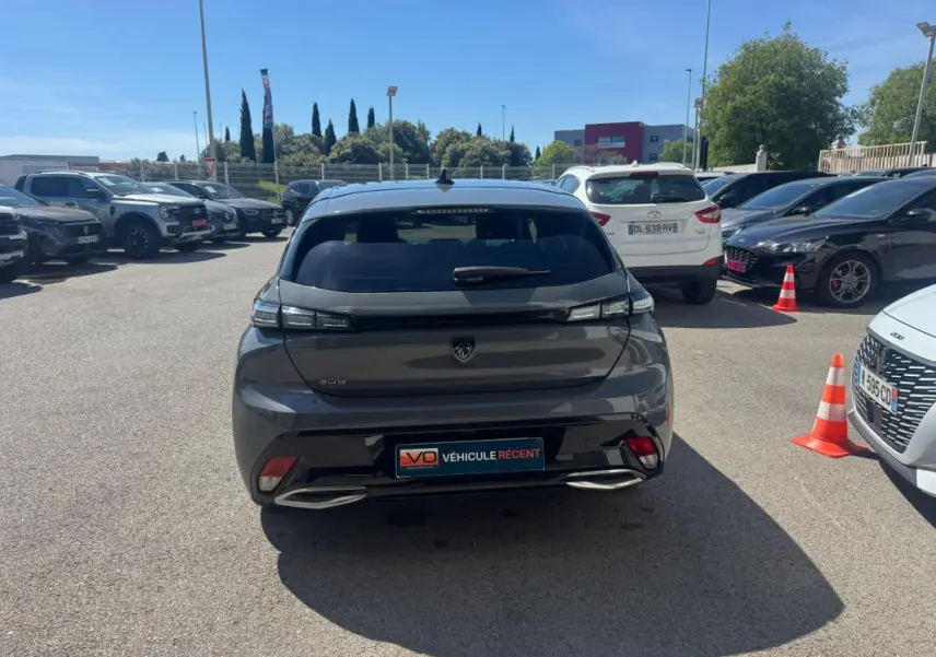 Vue arrière d'une Peugeot 308 Hybrid gris foncé stationnée en extérieur, avec feux arrière LED et double sortie d'échappement intégrée.