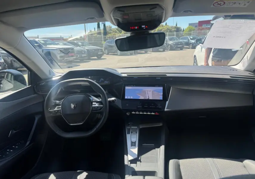 Vue intérieure avant de la Peugeot 308 Hybrid 136 e-DCS6 Allure gris, avec volant compact et écran tactile central lumineux.