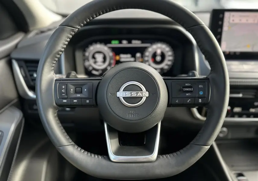 Volant cuir noir de Nissan Qashqai 2025 vu de face avec commandes intégrées et tableau de bord numérique flou en arrière-plan.