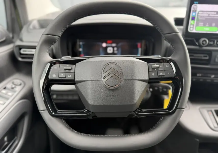 Vue rapprochée du volant cuir multifonctions noir de la Citroën Berlingo Multispace 2026, avec tableau de bord numérique en arrière-plan.