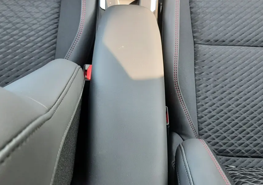Vue rapprochée de l'accoudoir central noir entre les sièges avant en tissu noir avec surpiqûres rouges de la Renault Clio VI.
